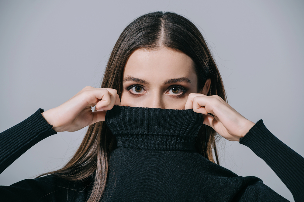 Portrait mode d’une femme cachant partiellement son visage avec un col roulé noir
