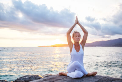 Femme méditant au bord de l’océan au coucher du soleil, en pleine reconnexion à elle-même