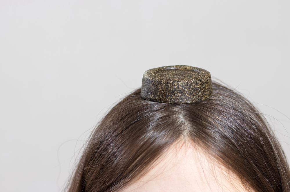 Shampoing solide posé sur la tête d’une femme, cheveux bruns lisses