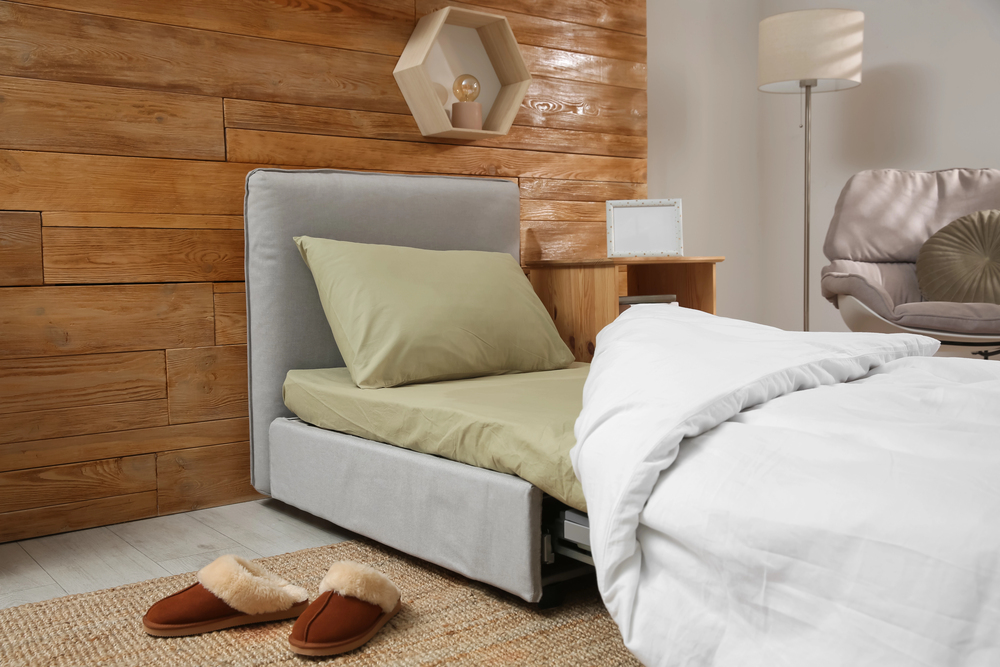 Canapé convertible gris clair transformé en lit confortable avec draps et coussins dans un intérieur bois chaleureux