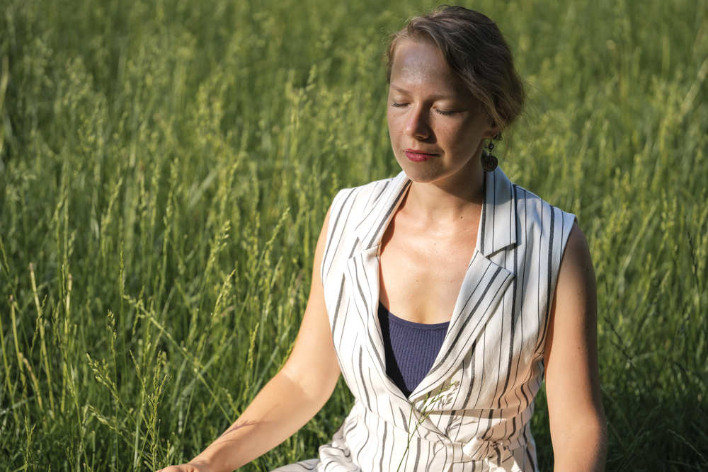 Femme méditant en pleine nature dans un champ, reconnectée à son souffle intérieur