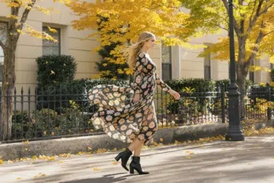 Femme élégante marchant en extérieur, robe midi fluide fleurie, bottines en cuir noir, ambiance automne chic, lumière naturelle douce.