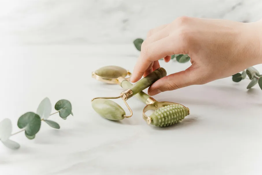 Main féminine saisissant un rouleau de jade pour massage facial, accessoire emblématique des rituels de soin coréens naturels