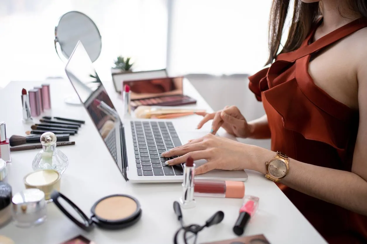 Consommatrice achetant du maquillage en ligne avec ses produits de beauté posés près de l’ordinateur