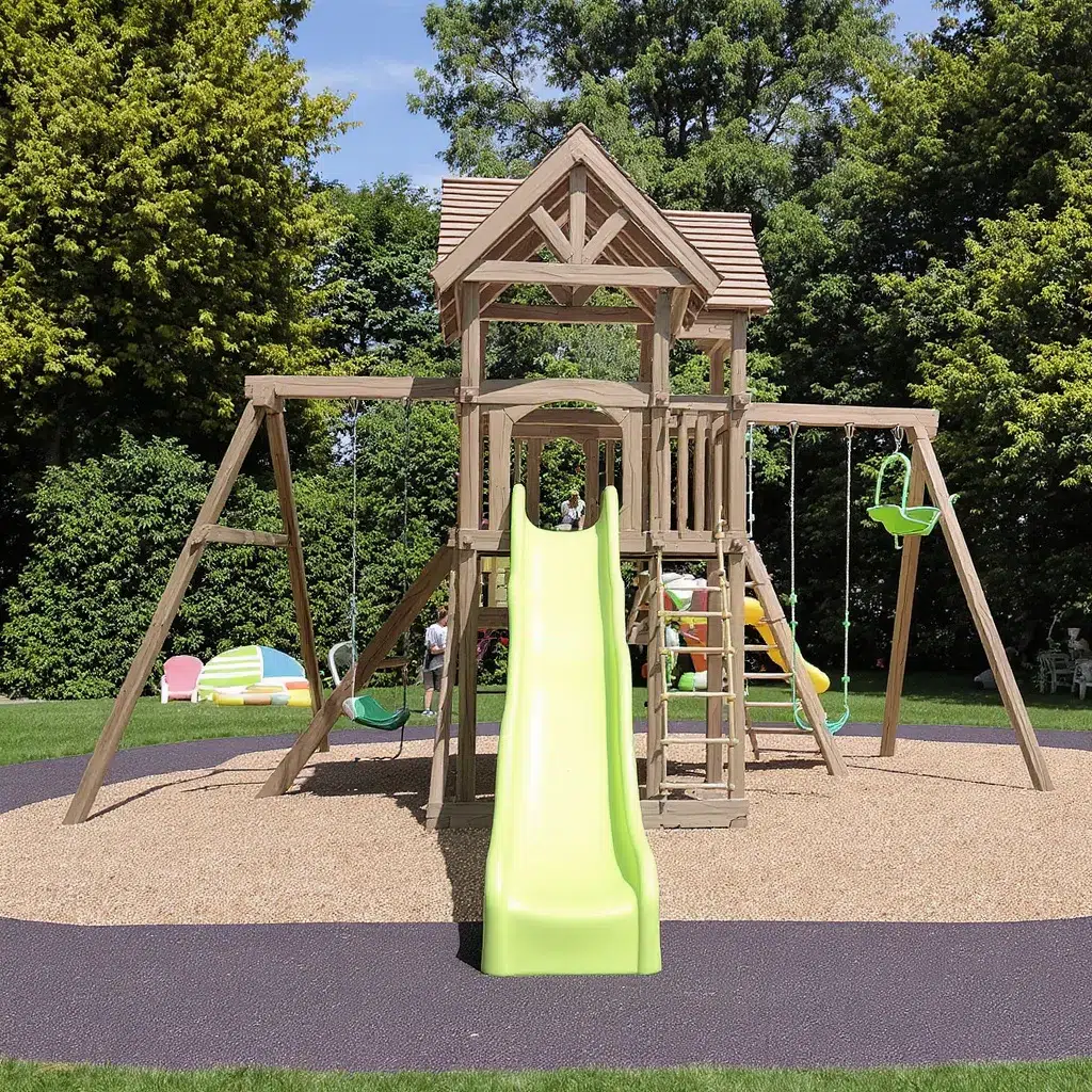 Aire de jeux en bois avec toboggan, installée sur un sol amortissant en gazon et dalles de sécurité colorées. Vue large, ambiance familiale.