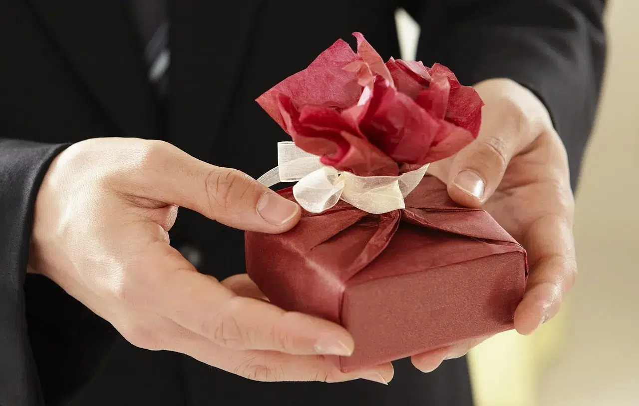 Mains d'homme offrant un cadeau soigneusement emballé de papier rouge avec une fleur décorative élégante.