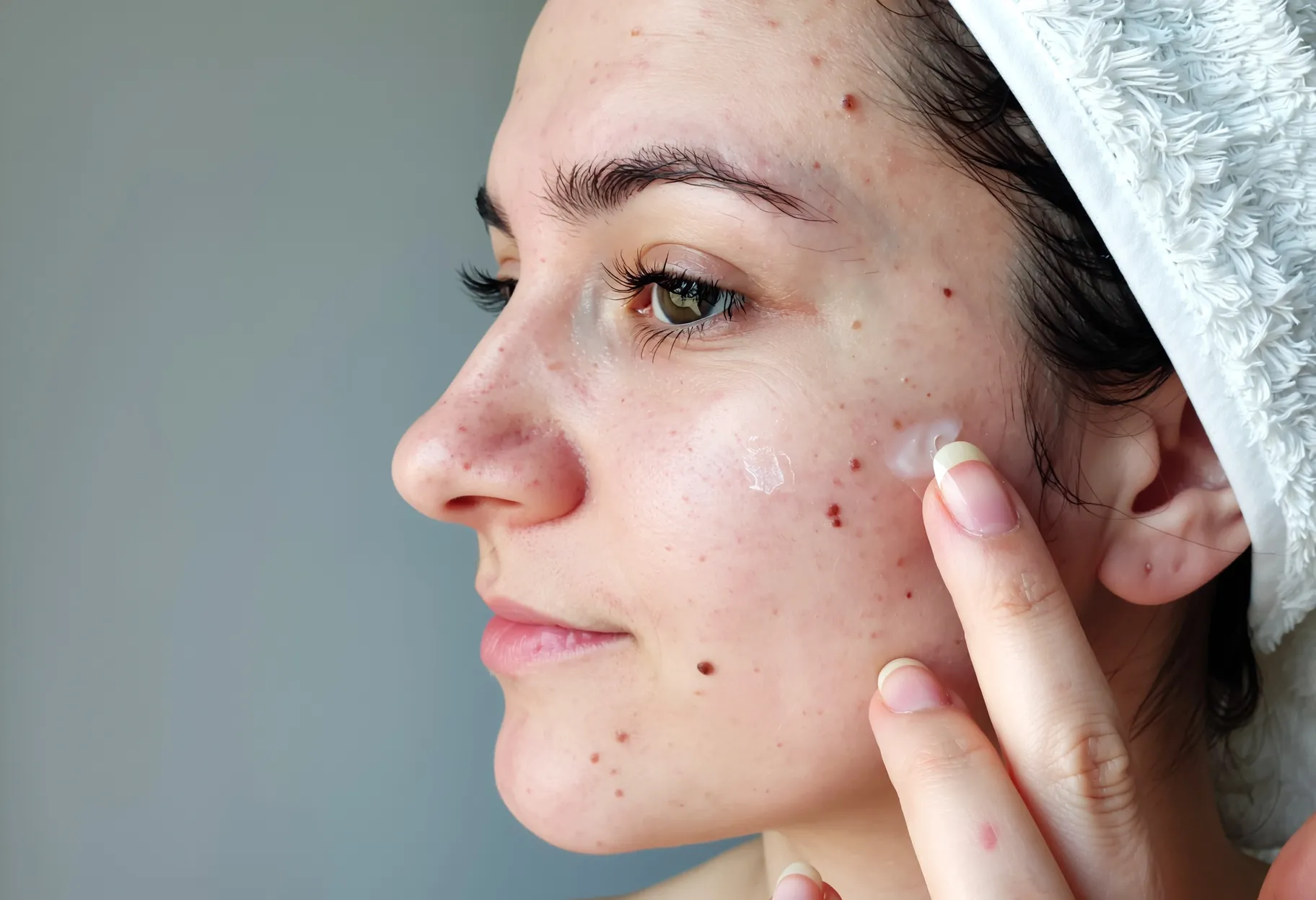 jeune femme appliquant un sérum anti-imperfections sur son visage devant un miroir, lumière douce.
