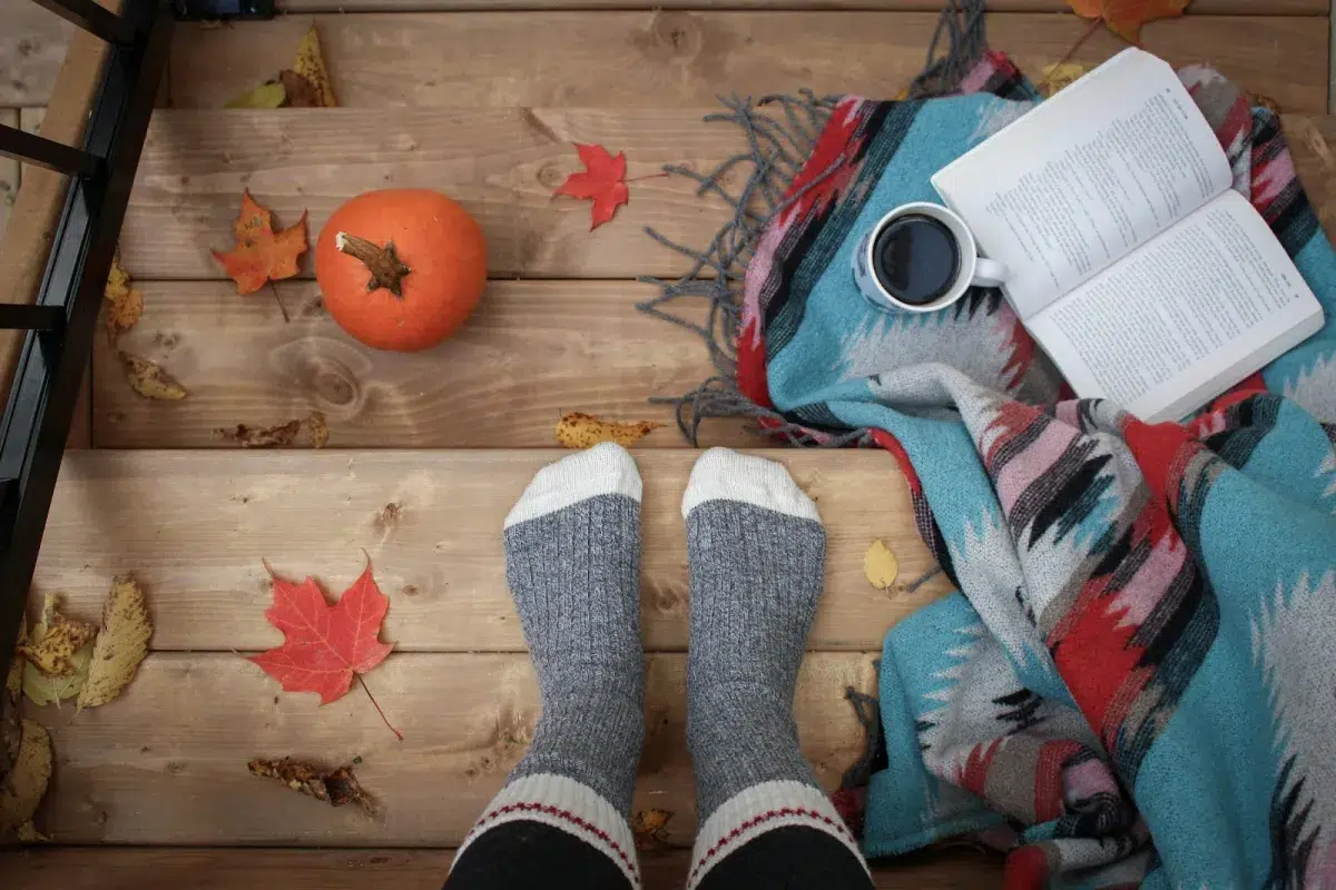 Ambiance cocooning d’automne avec plaid coloré, chaussettes chaudes d'enfant, boisson chaude et livre posé sur une terrasse en bois