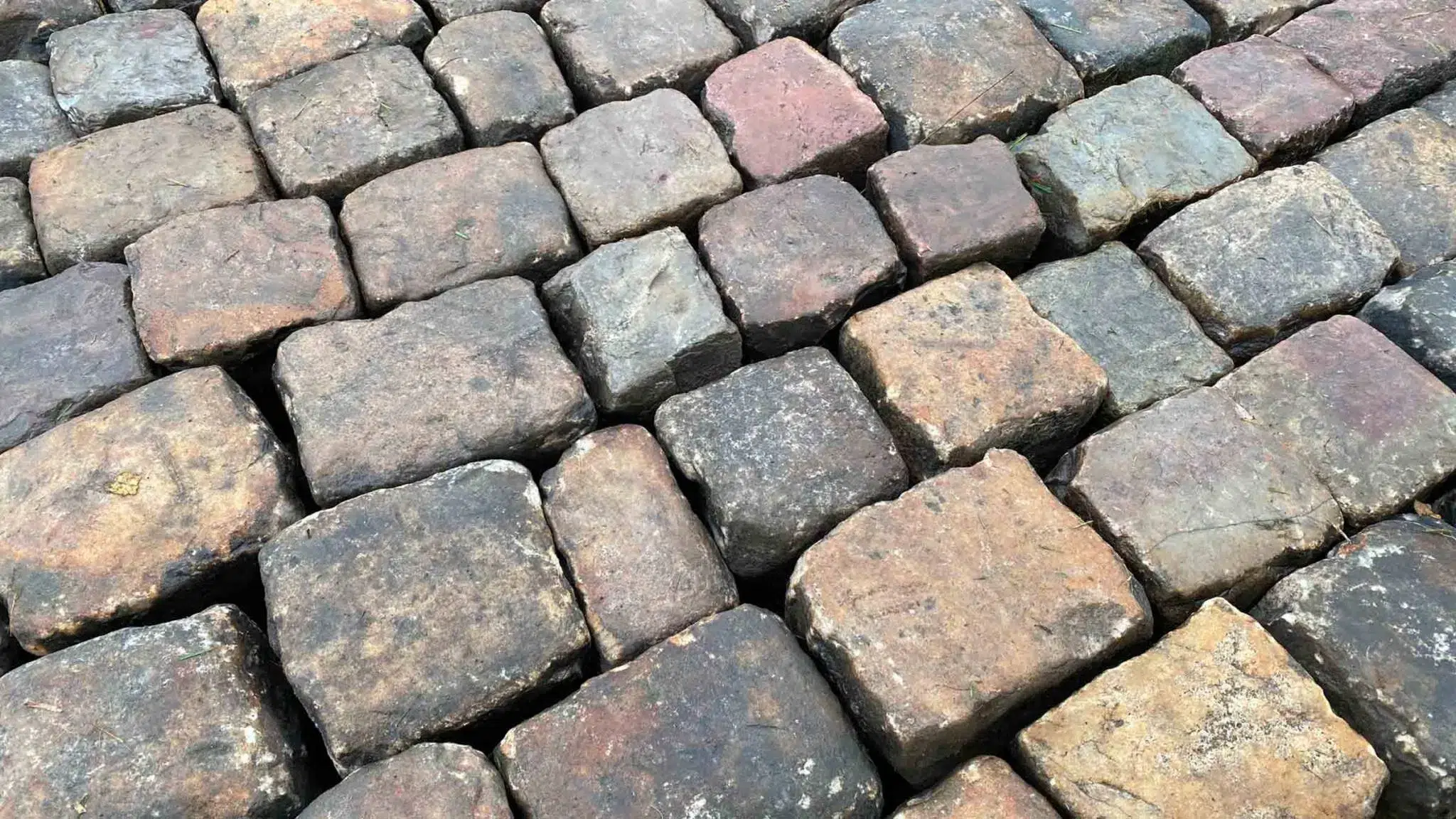 Détail de pavés anciens en pierre naturelle avec patine et teintes variées, apportant authenticité et charme au sol extérieur
