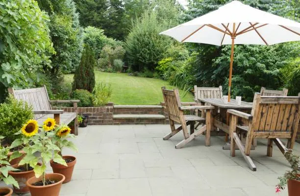 Un parasol adapté aux besoins de son jardin,protégeant une table en bois sur terrasse verdoyante entourée de plantes
