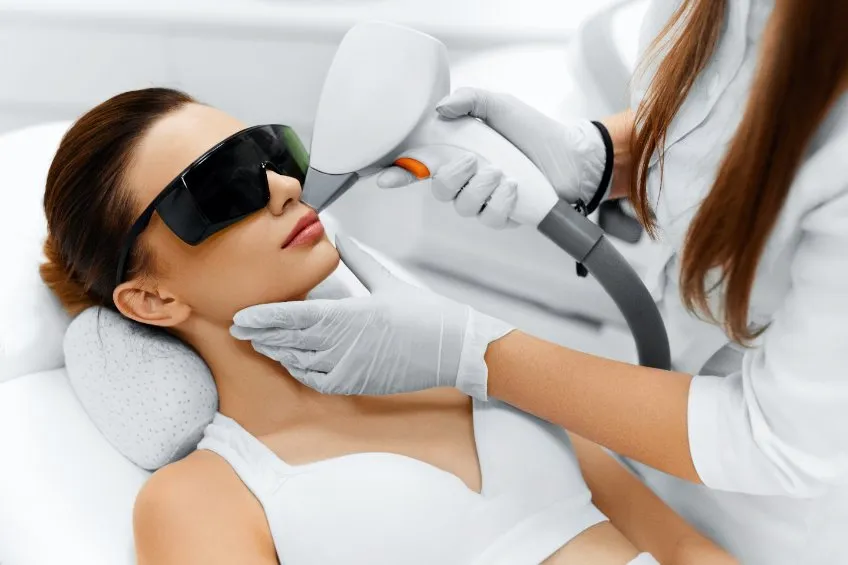 Femme allongée recevant un soin du visage professionnel avec appareil lumineux, protection oculaire et ambiance zen.