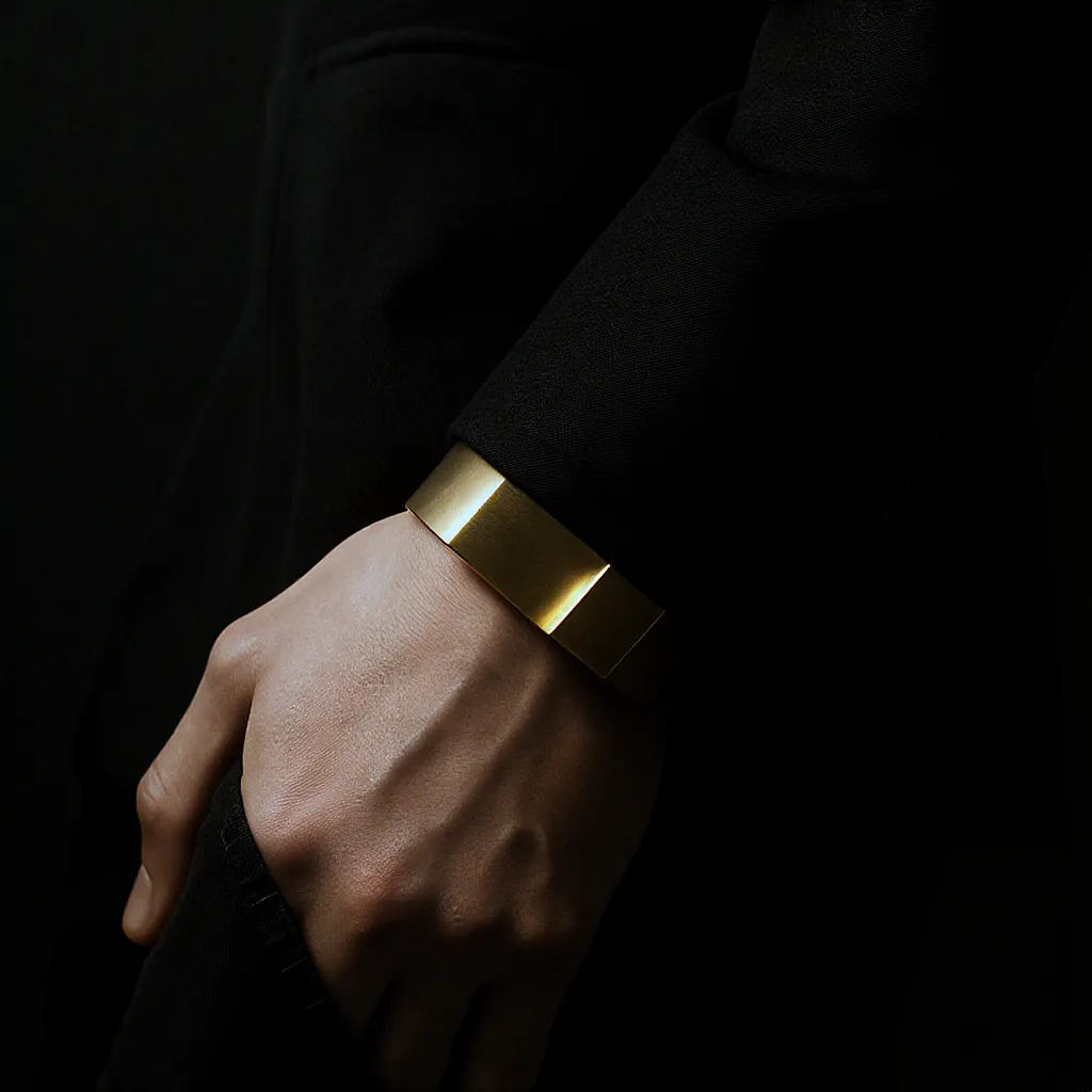 Gros plan sur une manchette géométrique dorée portée avec un blazer noir, lumière studio contrastée
