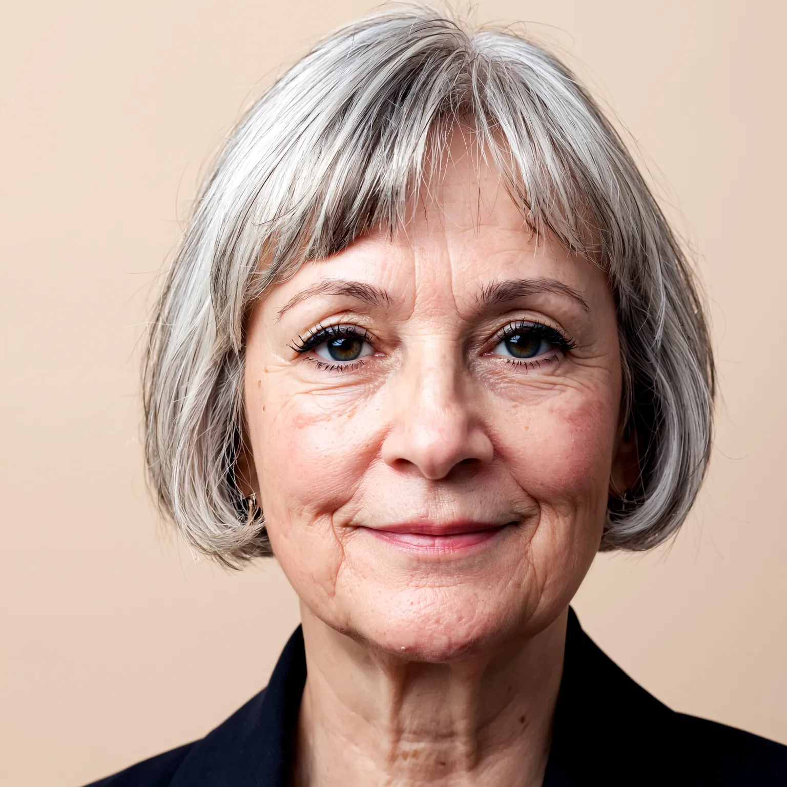 Femme de 60 ans avec coupe pixie classique et frange floue, coiffure grise douce et élégante pour affiner les traits.