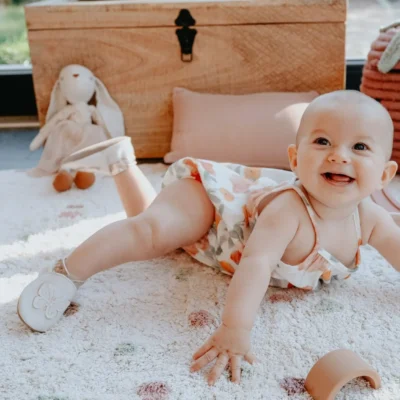 bébé souriant portant des chaussons souples sur un tapis de jeu