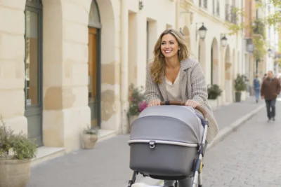 Jeune maman marchant dans une rue calme avec une poussette moderne adaptée à un usage quotidien en ville