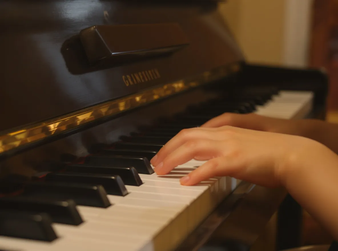 Mains d’un enfant jouant les premières notes sur un piano droit compact dans une ambiance douce et chaleureuse.