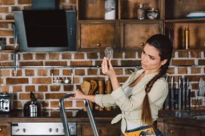 Femme ajustant des installations électriques dans une cuisine rustique durant la rénovation et l’ajout de nouveaux équipements.