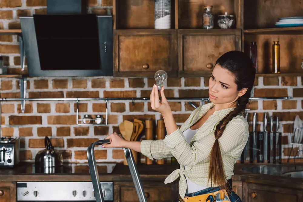 Femme ajustant des installations électriques dans une cuisine rustique durant la rénovation et l’ajout de nouveaux équipements.