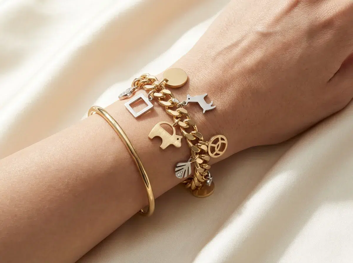 Photo bijou haut de gamme, bracelet breloques contemporain, maillons visibles, charms graphiques minimalistes, porté au poignet avec un jonc fin