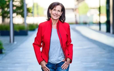 Femme de 55 ans portant une veste rouge vif et un jean brut, photographiée en lumière naturelle urbaine, style affirmé et moderne