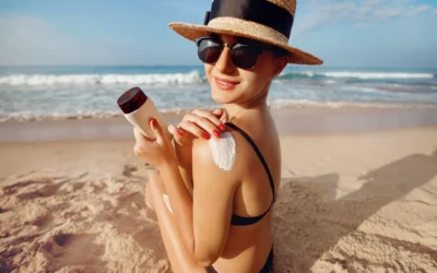 Femme avec chapeau de paille et lunettes de soleil appliquant un écran solaire sur l'épaule à la plage, combo protection solaire complète.
