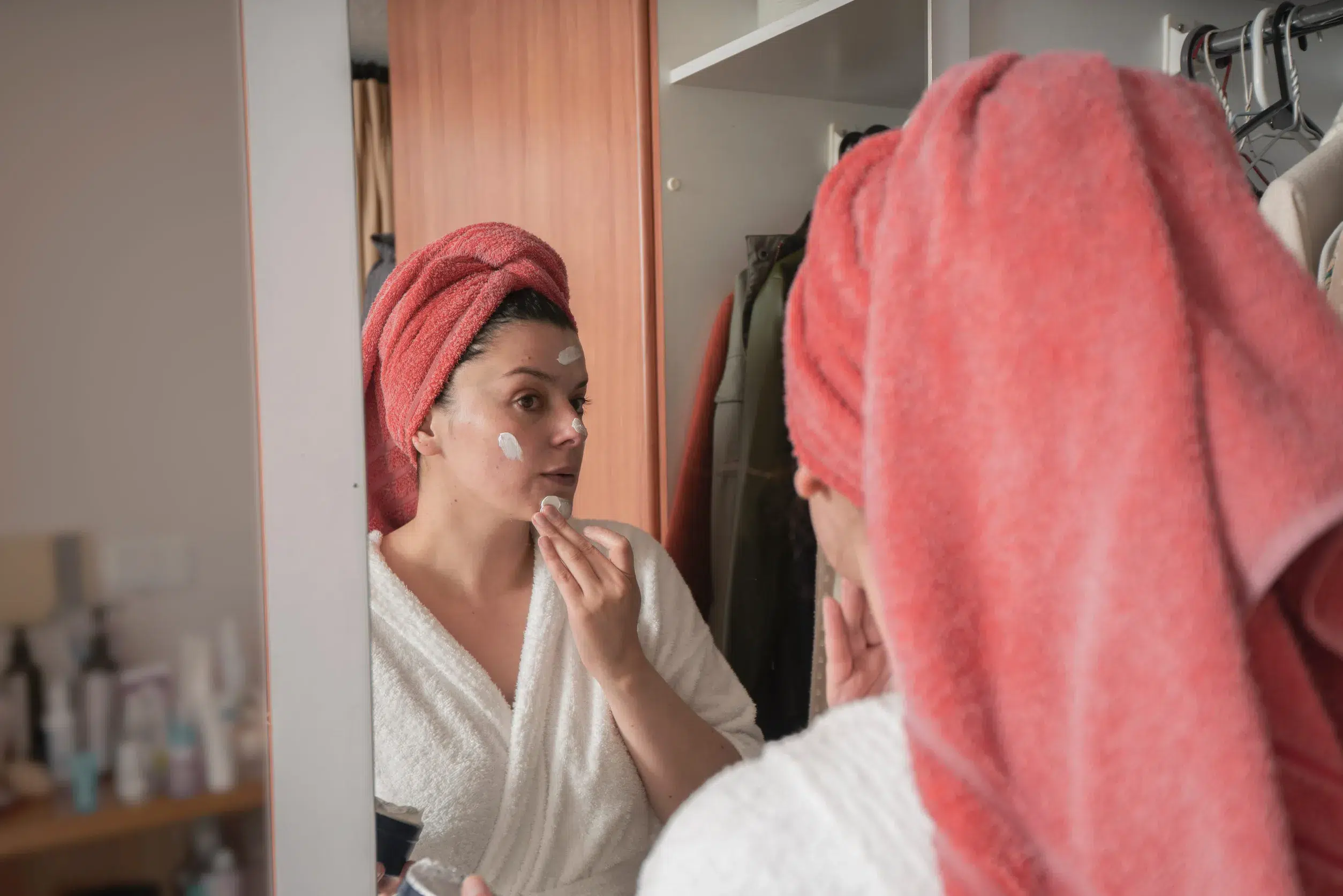 femme devant son miroir qui applique une creme sur son visage et qui ne sait plus quels soins visages choisir car sa peau est seche