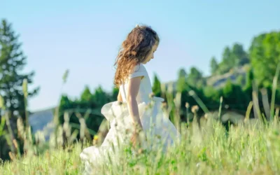 Petite fille en robe blanche de communion dans un champ fleuri au printemps