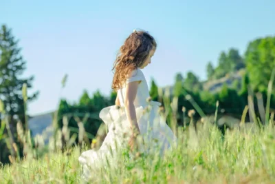 Petite fille en robe blanche de communion dans un champ fleuri au printemps