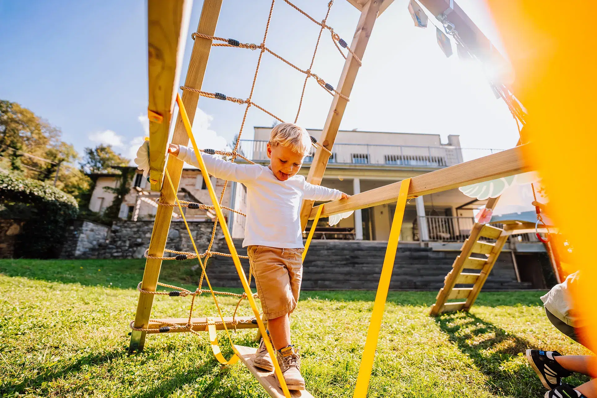 Enfant de 3 ans escaladant un filet de corde sur une structure de jeu en bois dans le jardin