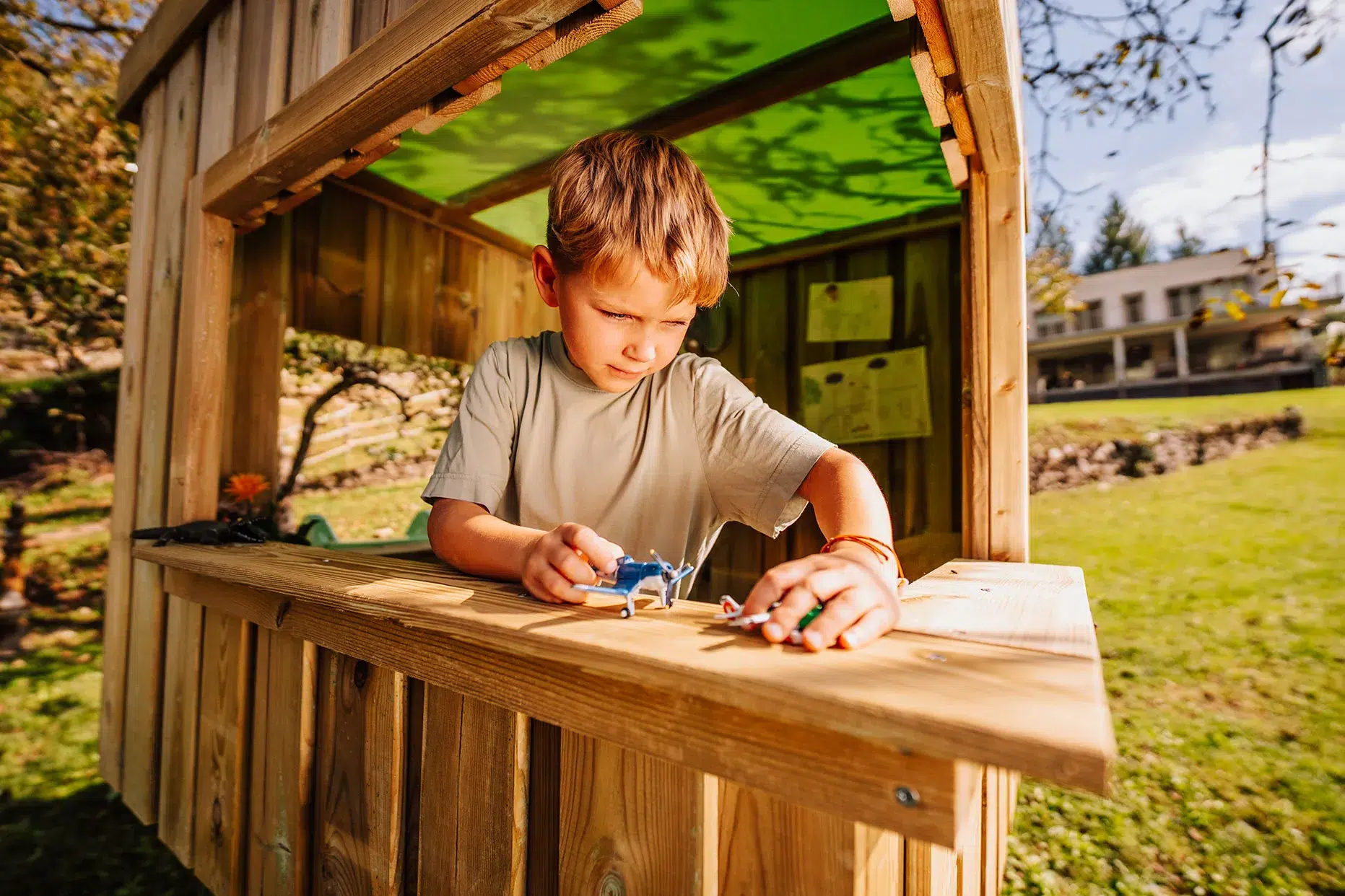 Enfant concentré jouant seul dans une cabane en bois au jardin, jeu libre et créatif
