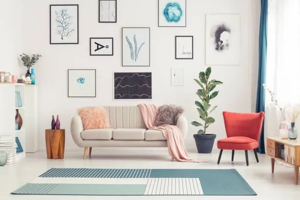 Salon moderne blanc avec canapé beige, fauteuil rouge vif et mur de cadres.