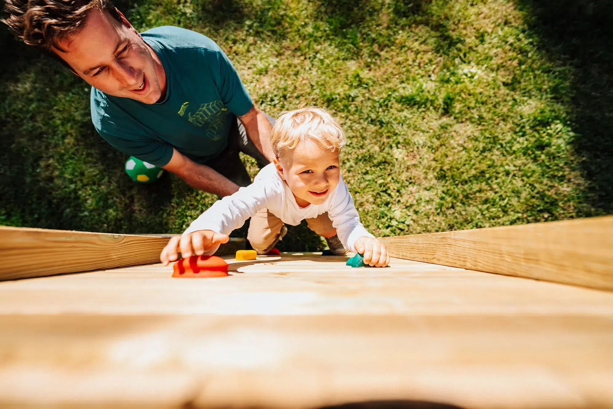 papa accompagnant son tout-petit sur un mur d'escalade en bois au jardin, premiers pas en escalade