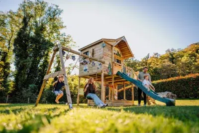 Famille jouant sur un portique en bois Wickey avec cabane, toboggan et balançoires dans un jardin