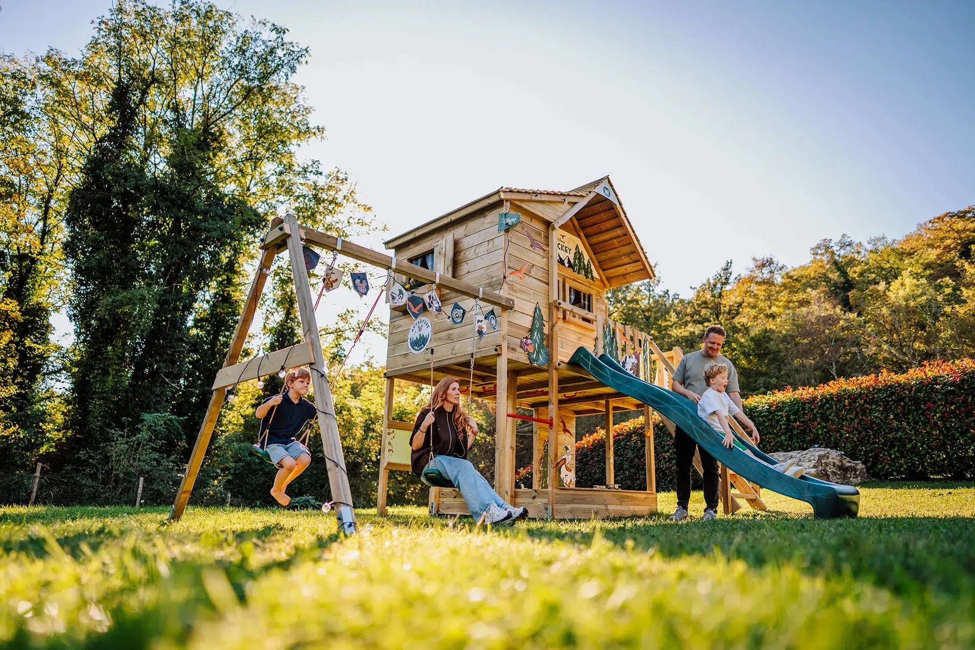Famille jouant sur un portique en bois Wickey avec cabane, toboggan et balançoires dans un jardin