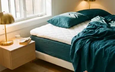 Lit défait avec surmatelas blanc épais et draps bleu canard, lumière du matin dans une chambre