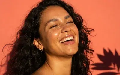 teint-terne-routine-glow-cover Femme souriante à la peau lumineuse en plein soleil, effet glow sans maquillage pour une routine anti-teint terne